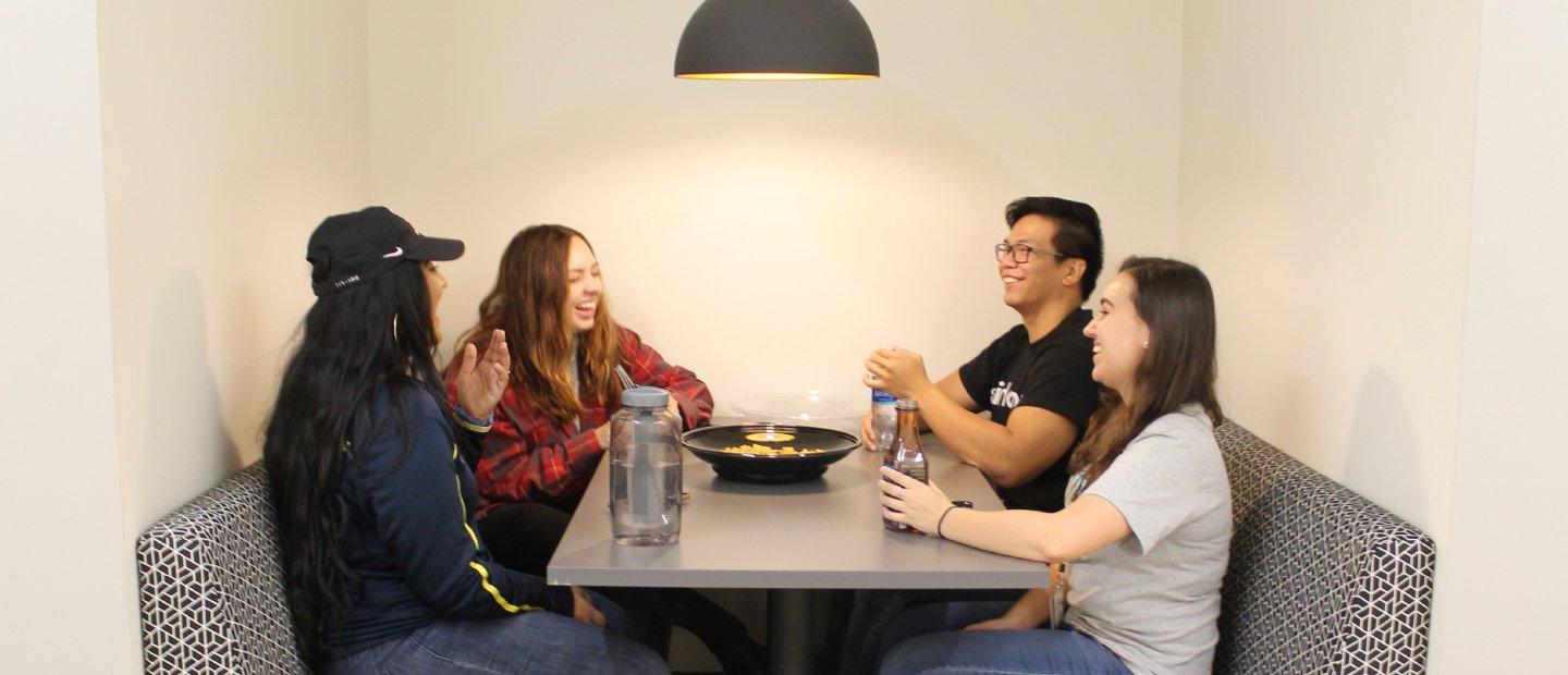 four students seated at a table with beverages and a bow of food in the middle